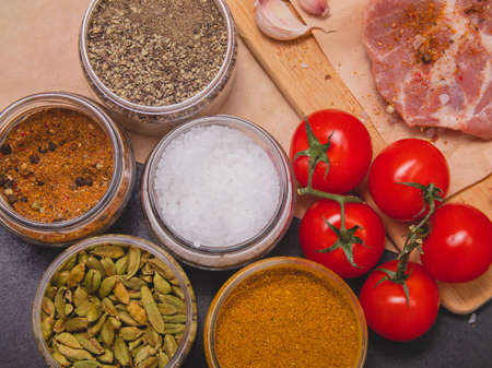 Raw beef steak with spices and cherry tomatoes on a dark slate, stone or concrete background. Top view with copy spaceの写真素材