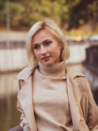 Close-up portrait of a beautiful girl in a beige coat with colorful autumn leaves. Beautiful model looks at the cameraの写真素材