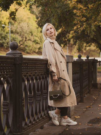 Close-up portrait of a beautiful girl in a beige coat with colorful autumn leaves. Beautiful model looks at the cameraの写真素材