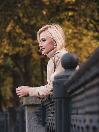 Close-up portrait of a beautiful girl in a beige coat with colorful autumn leaves. Beautiful model looks at the cameraの写真素材