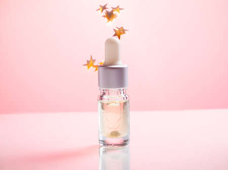 Amber glass bottles with golden stars on pink background. Natural organic cosmetic packaging, luxury beauty products for body care. amber bottle for essential oils and cosmeticsの写真素材