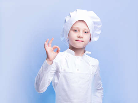 a 6 year old boy in a chef's suit and cap smiles at the camera and shows the OK signの写真素材