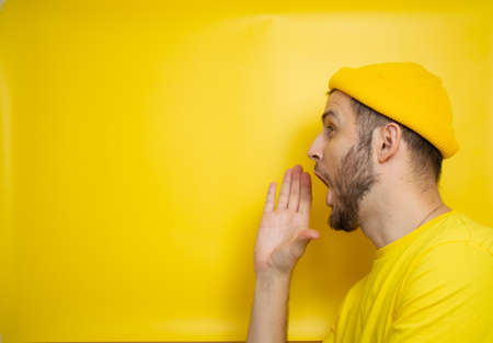 a man in a yellow T-shirt and a casual hat stands on a yellow background and shouts into an invisible gramophone. place for your textの写真素材