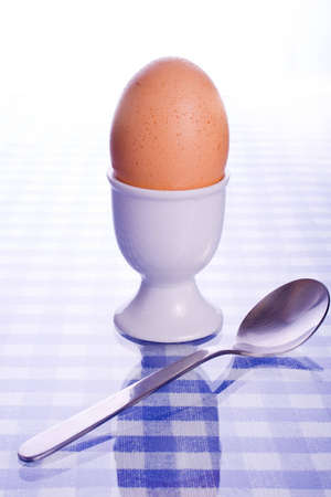 Soft boiled egg in egg cup with spoon reflected on blue check surface