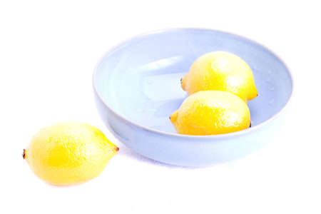 Fresh lemons in a blue bowl on whiteの写真素材