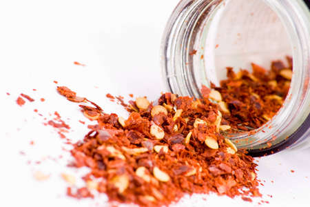 Crushed chilli spilling from glass container over whiteの写真素材
