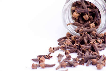 fresh cloves spilt from glass container over whiteの写真素材