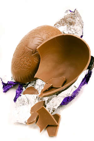A halved and broken Easter egg with wrapper over whiteの写真素材