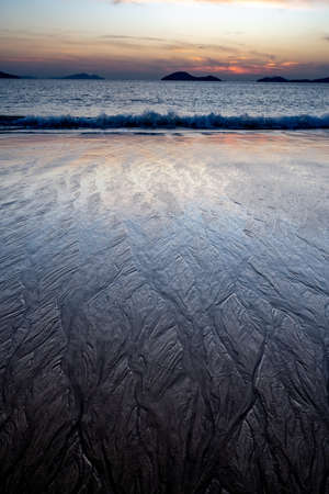 Magical morning seascape with rising Sun, water ripple and sand patterns, shallow, low tide.の写真素材