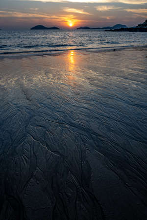 Magical morning seascape with rising Sun, water ripple and sand patterns, shallow, low tide.の写真素材