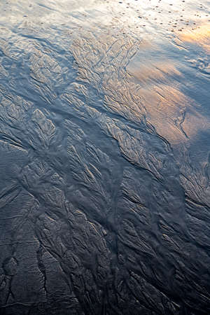Magical morning seascape with rising Sun, water ripple and sand patterns, shallow, low tide.の写真素材