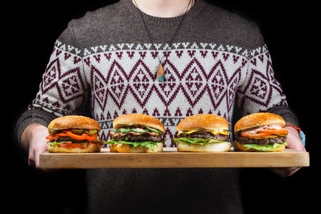 young guy holding a burgers on a wooden tray. black background.の写真素材
