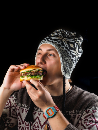 young man eating a fast food hamburger isolated on black.の写真素材