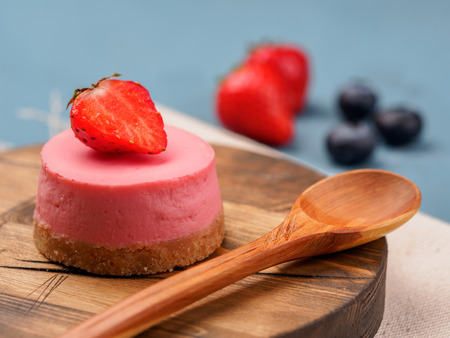 Small round strawberry cheesecakes on wooden desk and blue background.の写真素材