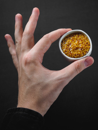 Grain mustard on gravy boat at hand. black background.の写真素材