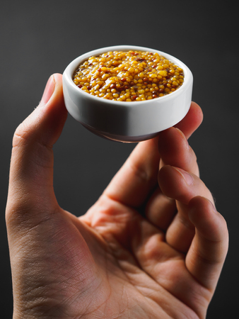 Grain mustard on gravy boat at hand. black background.の写真素材