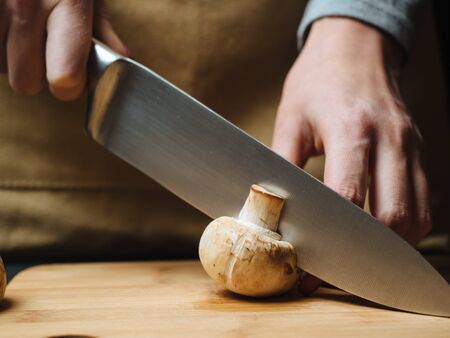 Woman cutting raw mushrooms on wooden board.の写真素材
