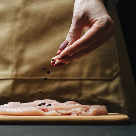 Woman hand sprinkle raw chicken fillet by condiment.の写真素材