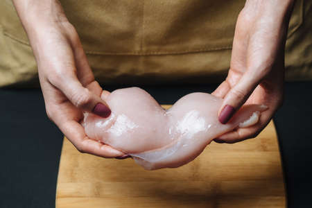 Raw chicken fillet in woman hands on black background.の写真素材