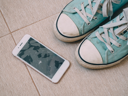 Broken screen smartphone on the tile floor with shoes.の写真素材