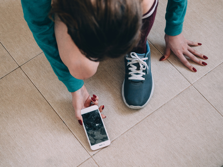 Girl with broken screen smartphone on the tile floor.の写真素材