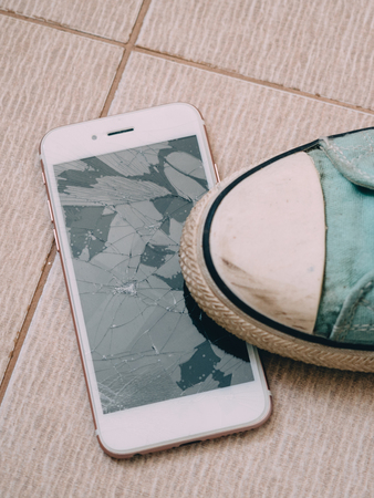 Broken screen smartphone on the tile floor with shoes.の写真素材