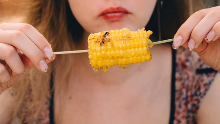 Young girl eating hot roast salt corn.の写真素材