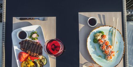 Beef steak with grilled vegetables and sushi rolls on the table.の写真素材