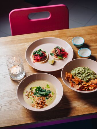 Nachos, guacamole, tacos, soup and candles on the table in cantina bar.