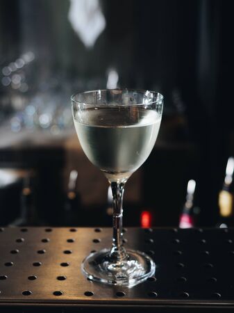 Clear alcohol cocktail in glass on bar counter.