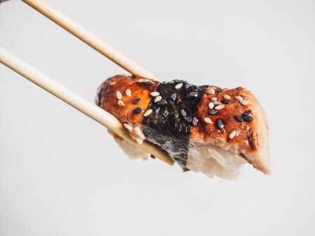 Sushi with eel rice in wooden chopsticks. White background.の写真素材