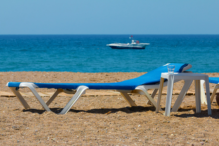 Sunbeds on rocky beach and parasailing speed boat waiting for customersの写真素材