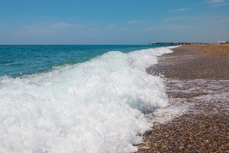 Long waves along rocky beach with pier in the distanceの写真素材
