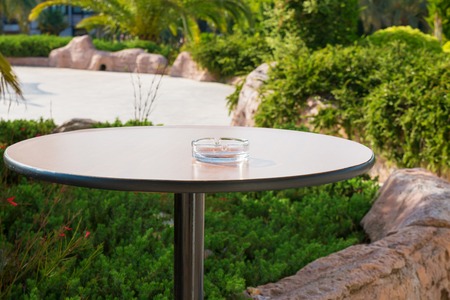 Empty ashtray on one legged, round table in the garden.の写真素材