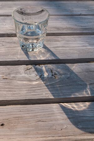 Glass of water casting shadow on wooden tableの写真素材