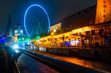 Restaurants, bars and pubs on Dusseldorf city street at night near embankment of Rhine river. Night cityscape with Ferris wheel and colorful illuminationの写真素材