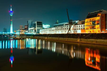 Night scene of Rhein river at night in Dusseldorf. View from Media harbor on Rheinturm tower, cafe on water and port crane with reflections at water; Night filterの写真素材