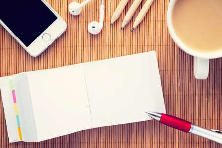 Workplace with opened empty notebook for notes. Coffee, smartphone, headphones and notepad on bamboo wooden background; Top view with copy space. Vintage filterの写真素材