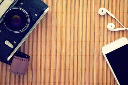 Top view on bamboo table with copy space; Retro film photo camera, smartphone and headphones laying on wooden background; Vintage styleの写真素材