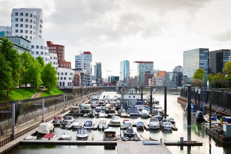 Cloudy day in Dusseldorf's harbour. Cityscape view on Medienhafen full of boatsの写真素材
