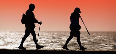 Silhouette of tourists walking along the shore at sunset tourism equipmentの写真素材