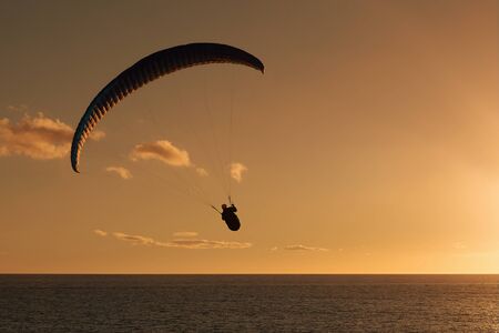 Paraglider flying at sunset over the oceanの写真素材
