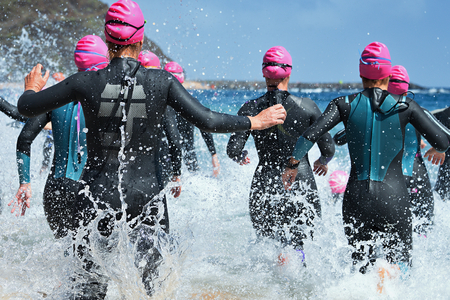 Group triathlon participants running into the water for swim portion of race,splash of water and athletes running.