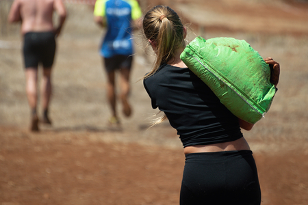 Mud race runners,young woman running with sandbagの写真素材