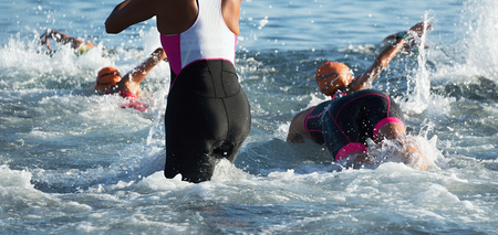 Group triathlon participants running into the water for swim portion of race,splash of water and athletes runningの写真素材