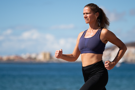 Athlete woman running in the beach at summer vacations exercise, training for marathon