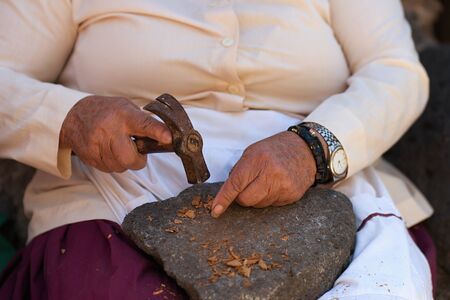 Grandma cracking nut almond shells with a hammer to collect the healthy almonds