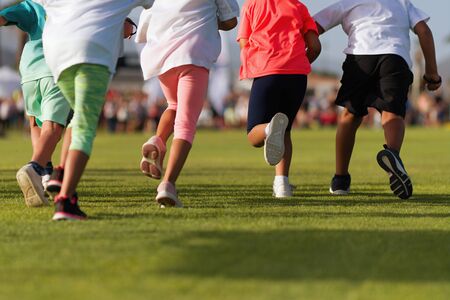Running children, young athletes run in a kids run race, running on grass detail on legs, running in the light of morningの写真素材