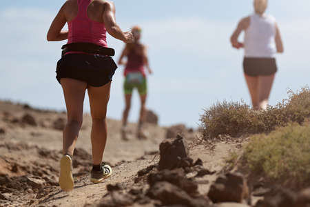 Runners running shoes on trail run. Ultra running athletes legs close up on running in rock path...