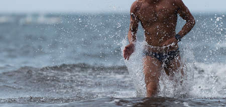 Swimmer running out of ocean finishing swim race.Fit man ending swimming sprinting determined out of waterの写真素材
